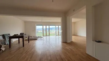 Geräumiger, offener Wohnbereich mit Holzboden und großen Fenstern, die viel Tageslicht hereinlassen und eine weite Aussicht bieten.