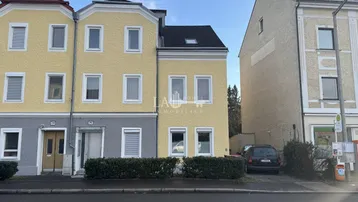 Mehrere Gebäude mit gelber und grauer Fassade an einer Straße mit Parkmöglichkeiten.