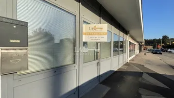 Außenansicht eines Geschäftsgebäudes mit großen Fenstern, Jalousien und einem Verkaufsschild.