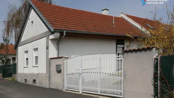 Vorderansicht eines Einfamilienhauses mit rotem Ziegeldach und weißem Einfahrtstor.