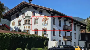 Traditionelles Gebäude mit bemalter Fassade, Holzbalkonen und Bergblick unter blauem Himmel.