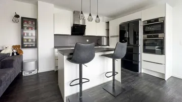 Moderne offene Küche mit Kochinsel, integrierten Geräten und dunklem Bodenbelag.