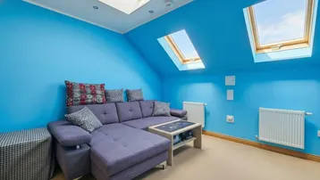 Helles Wohnzimmer im Dachgeschoss mit blauen Wänden, gemütlichem Sofa und mehreren Dachfenstern.