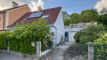 Hausfassade mit Gartenbereich, Zaun und Garage, die Renovierung benötigt.