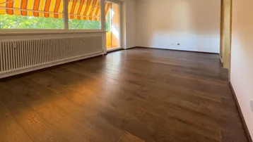 Helles Wohnzimmer mit dunklem Holzboden und Zugang zu einem Balkon mit Markise.
