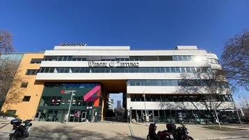 Moderne Bürogebäude-Fassade mit großen Fenstern und einem Durchgang, beleuchtet von der Sonne.
