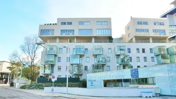 Modernes Wohngebäude mit vielen Fenstern und Balkonen, umgeben von Grünflächen und einer Straße.