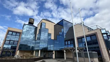 Moderne Geschäftsfassade mit großen Glasflächen und beigen Paneelen unter einem bewölkten Himmel.