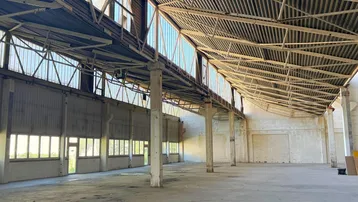 Geräumige Industriehalle mit hoher Decke, sichtbaren Trägern und vielen Fenstern, die viel Tageslicht hereinlassen.