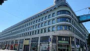 Modernes Geschäftsgebäude mit mehreren Etagen, großen Fenstern und Ladenflächen im Erdgeschoss an einer belebten Straße.