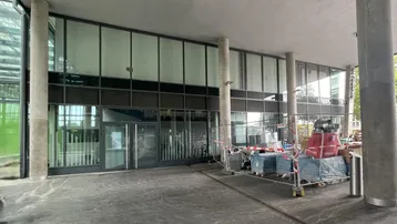Moderne Gebäudefassade mit großen Glasflächen und einem Eingangsbereich, der sich noch im Bau befindet.