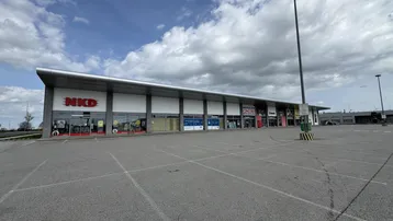 Modernes Geschäftsgebäude mit großem Parkplatz unter bewölktem Himmel, ideal für Einzelhandel.