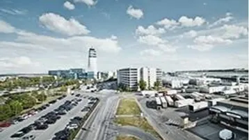 Weitläufige Außenansicht eines Gewerbegebiets mit Bürogebäuden, großem Parkplatz und Zufahrtsstraßen unter blauem Himmel.