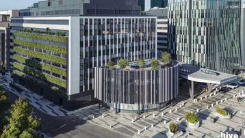 Moderne Bürogebäude mit vertikalen Gärten und einer markanten runden Fassade in einer städtischen Umgebung.