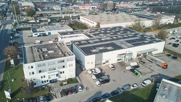 Luftaufnahme eines Industriegebiets mit mehreren Gebäuden, Parkplätzen und Solaranlagen auf den Dächern.