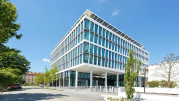 Modernes Bürogebäude mit weißer Fassade, großen Fenstern und Solarpaneelen auf dem Dach.