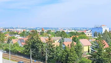 Weitblick über eine Wohnsiedlung mit vielen Bäumen, Bahngleisen und einer Stadtkulisse am Horizont.