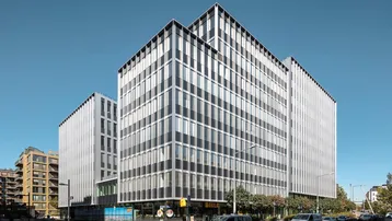 Modernes Bürogebäude mit Glasfassade und vertikalen Lamellen an einem sonnigen Tag in der Stadt.