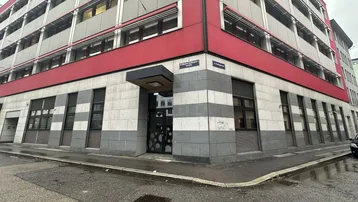 Modernes Bürogebäude an einer Straßenecke mit roter und grauer Fassade sowie vielen Fenstern.