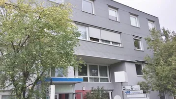 Modernes Bürogebäude mit geriffelter Fassade, großen Fenstern und Bäumen im Vordergrund.