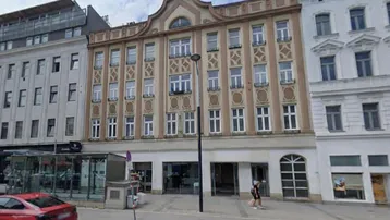 Historisches Gebäude mit reich verzierter Fassade und Geschäften im Erdgeschoss an einer belebten Straße.
