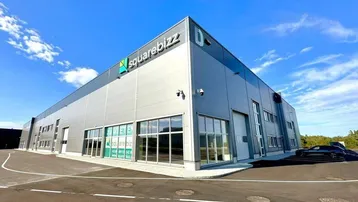 Moderne Gewerbehalle mit großen Glasfronten und dem Firmenlogo 'squarebizz' an der Fassade unter blauem Himmel.