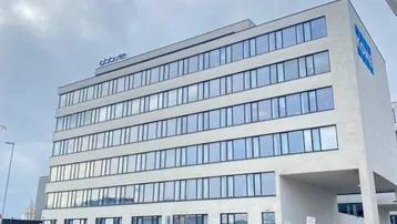 Modernes Bürogebäude mit vielen Fenstern und einer klaren Architektur unter bewölktem Himmel.