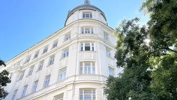 Historisches Gebäude mit weißer Fassade, runder Eckarchitektur und vielen Fenstern unter blauem Himmel.