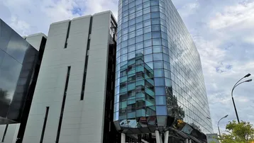 Moderne Architektur mit einer markanten Glasfassade und einem strukturierten Gebäude unter bewölktem Himmel.