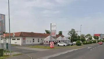 Panoramablick auf eine Geschäftsstraße mit einem KiK-Laden, Parkplätzen und umliegenden Gebäuden unter bewölktem Himmel.