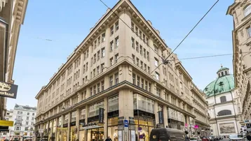 Historisches Eckgebäude mit vielen Fenstern und Geschäften im Erdgeschoss in einer belebten Stadtstraße.