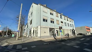 Außenansicht eines Geschäftsgebäudes an einer Straßenecke mit Straßenbahnschienen und blauer Fassade.