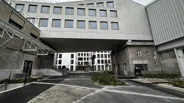 Moderne Architektur mit einem Durchgang zu einem Innenhof, umgeben von verschiedenen Gebäudeteilen.