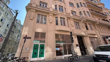 Historisches Gebäude an einer Straßenecke mit klassischer Architektur und Geschäften im Erdgeschoss.