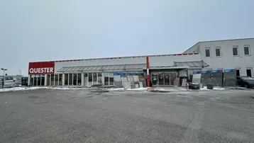 Außenansicht des Quester-Gebäudes mit großem Parkplatz und leichter Schneedecke im Winter.