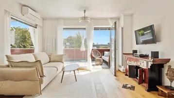 Helles Wohnzimmer mit beigem Sofa, Holzboden und Zugang zu einem sonnigen Balkon.