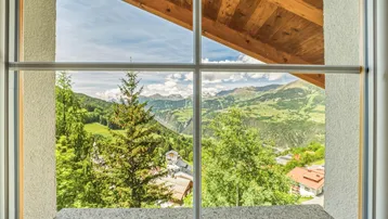 Panoramablick aus dem Fenster auf die umliegende grüne Berglandschaft und das Tal.