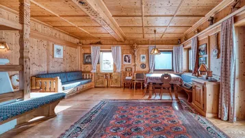 Gemütlicher Wohn-Essbereich im alpinen Stil mit viel Holzvertäfelung und traditionellem Teppich.