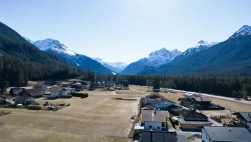 Weitläufige Luftaufnahme eines Tals mit einem Dorf, Feldern und schneebedeckten Bergen in der Ferne.