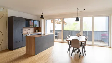 Offener Wohn-Essbereich mit moderner Küche, Kücheninsel und Zugang zum Balkon.