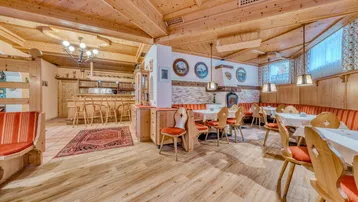 Geräumiger Speisesaal mit Holzbalkendecke, rustikalen Tischen und einem Kamin im Hintergrund.