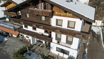 Traditionelles Gebäude im alpinen Stil mit Holzbalkonen und verschneitem Dach in bergiger Umgebung.