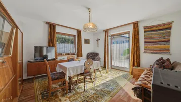 Gemütlicher Wohn-Essbereich mit traditionellen Holzmöbeln, Teppichboden und Zugang zur Terrasse.