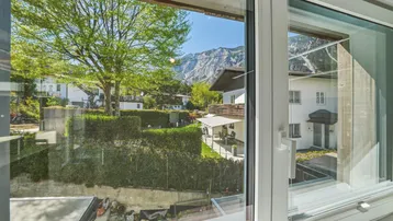 Panoramablick aus dem Fenster auf die Berge und die grüne Umgebung mit weiteren Häusern.