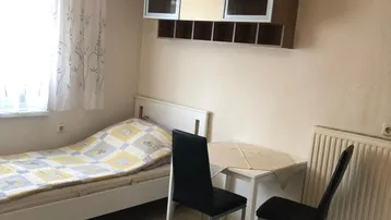 Helles Schlafzimmer mit Einzelbett, kleinem Esstisch und Hängeschränken, ideal für ein Studio-Apartment.