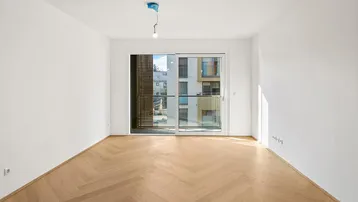 Helles Zimmer mit Fischgrätparkett und Zugang zu einem Balkon, bietet Blick auf umliegende Gebäude.