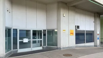 Eingangsbereich eines Geschäftsgebäudes mit großen Glasfronten und moderner Betonarchitektur.
