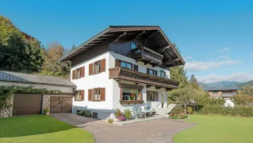 Traditionelles Chalet mit weißer Fassade, Holzbalkonen, Doppelgarage und gepflegtem Garten mit Bergblick.
