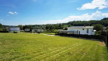Weitläufiges grünes Grundstück mit Blick auf umliegende Häuser und die hügelige Landschaft unter blauem Himmel.