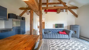 Wohnbereich mit sichtbaren Holzbalken, einem bequemen blauen Sofa und einem Kaminofen.